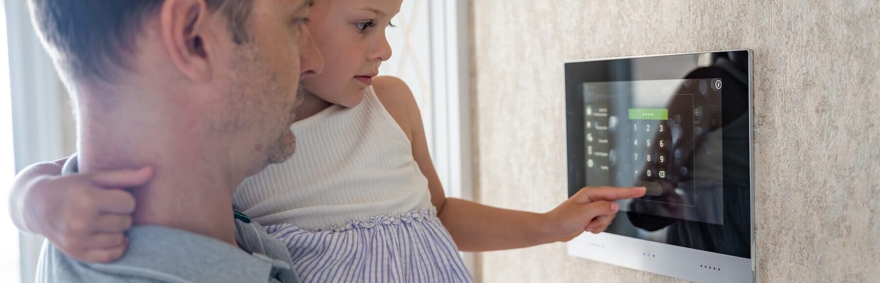 Daughter in her father's arms using security tablet panel on wall