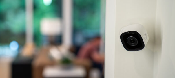 Security camera on the wall inside of a home while family spends time in the living room
